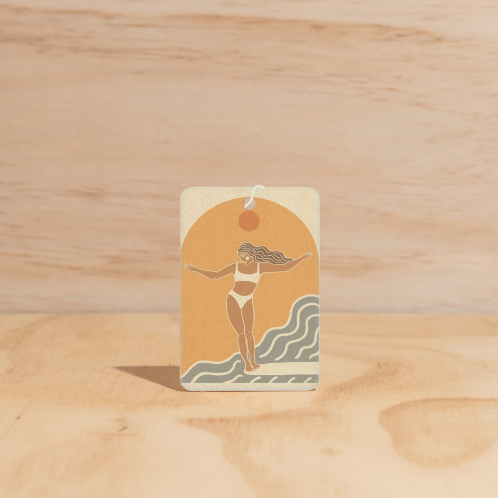 The Commonfolk air freshener features a beige and orange color scheme with a graphic of a woman in a bikini with outstretched arms above a wave design.