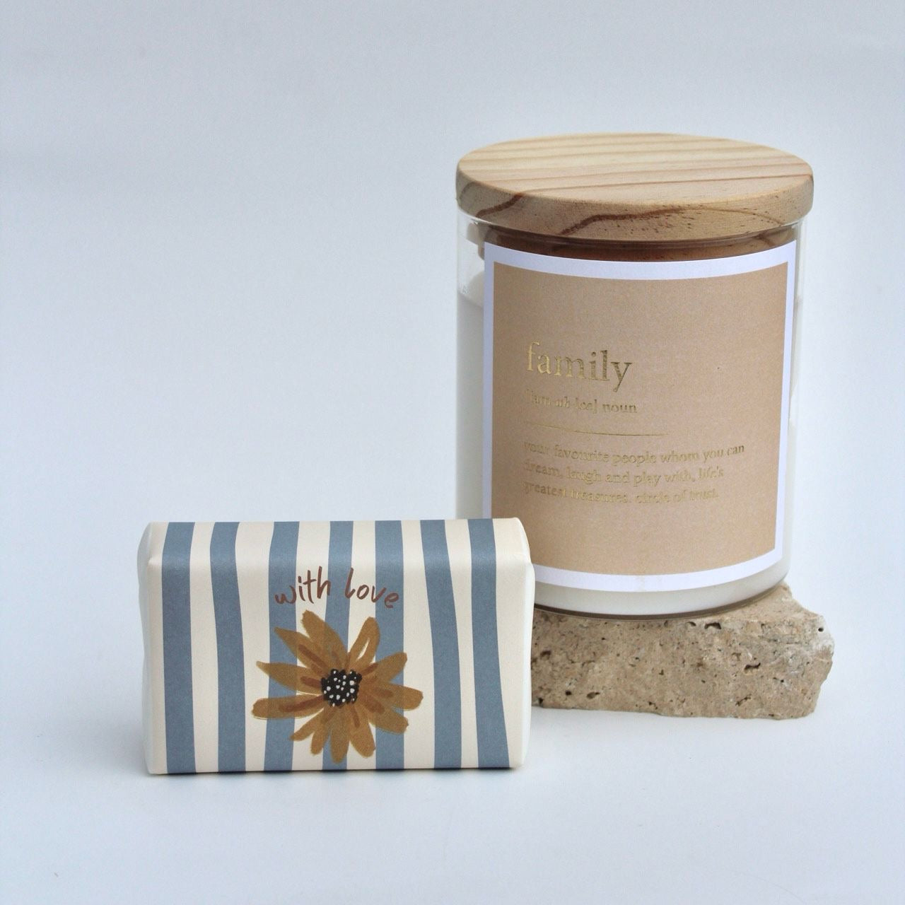 A gift set including a scented candle in a glass jar with the text 'family' and a wooden lid, a body bar with blue and white stripes, all displayed on a white background.