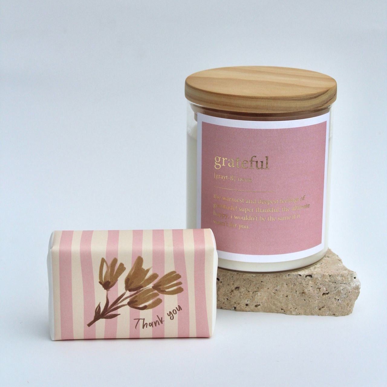 The Commonfolk gift set includes a clear candle jar with a wooden lid labeled 'grateful', a striped body bar with 'Thank you' printed on it, all displayed on a stone surface.