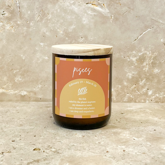 The Commonfolk scented soy wax candle has a label indicating it is a 'Pisces' themed candle, featuring a beige and orange label with text and decorative elements.