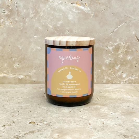 The Commonfolk scented candle with a wooden lid and amber glass jar has the label 'Aquarius', the zodiac sign, with a date range of January 20 to February 18.
