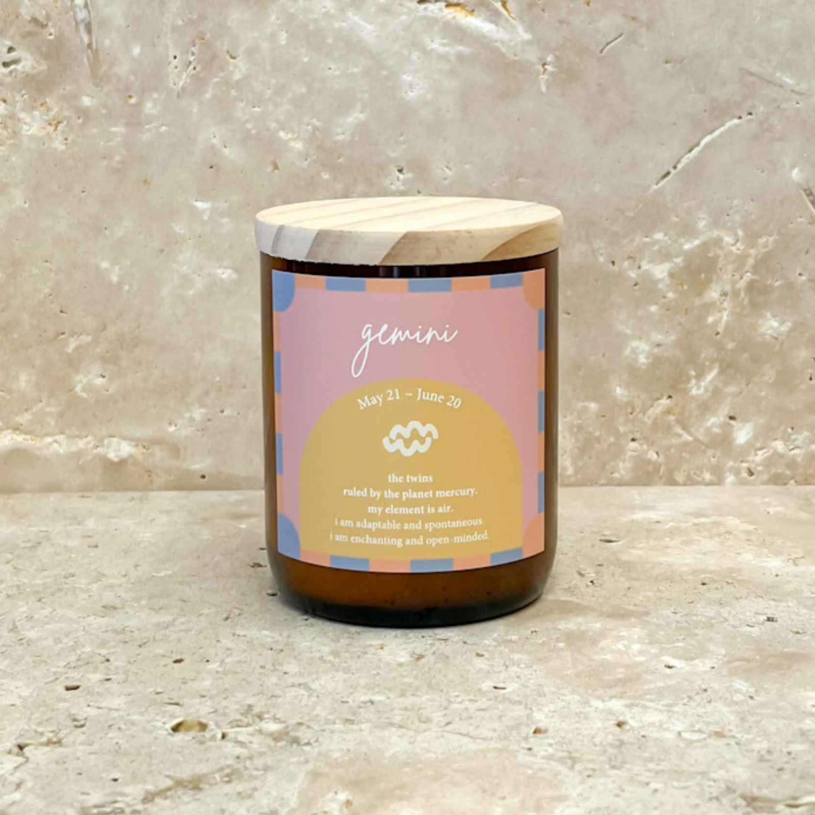 The Commonfolk scented soy wax candle with a wooden lid, in an amber jar, labeled 'Gemini' with a date range of May 21 - June 20, and featuring a yellow and blue color scheme.