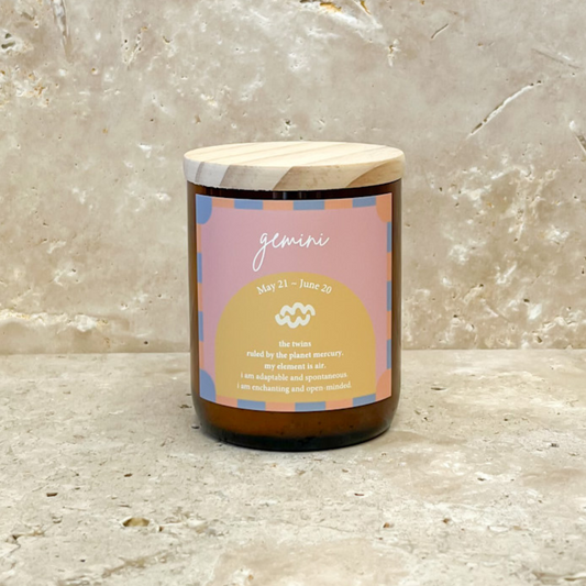 The Commonfolk scented soy wax candle with a wooden lid, in an amber jar, labeled 'Gemini' with a date range of May 21 - June 20, and featuring a yellow and blue color scheme.