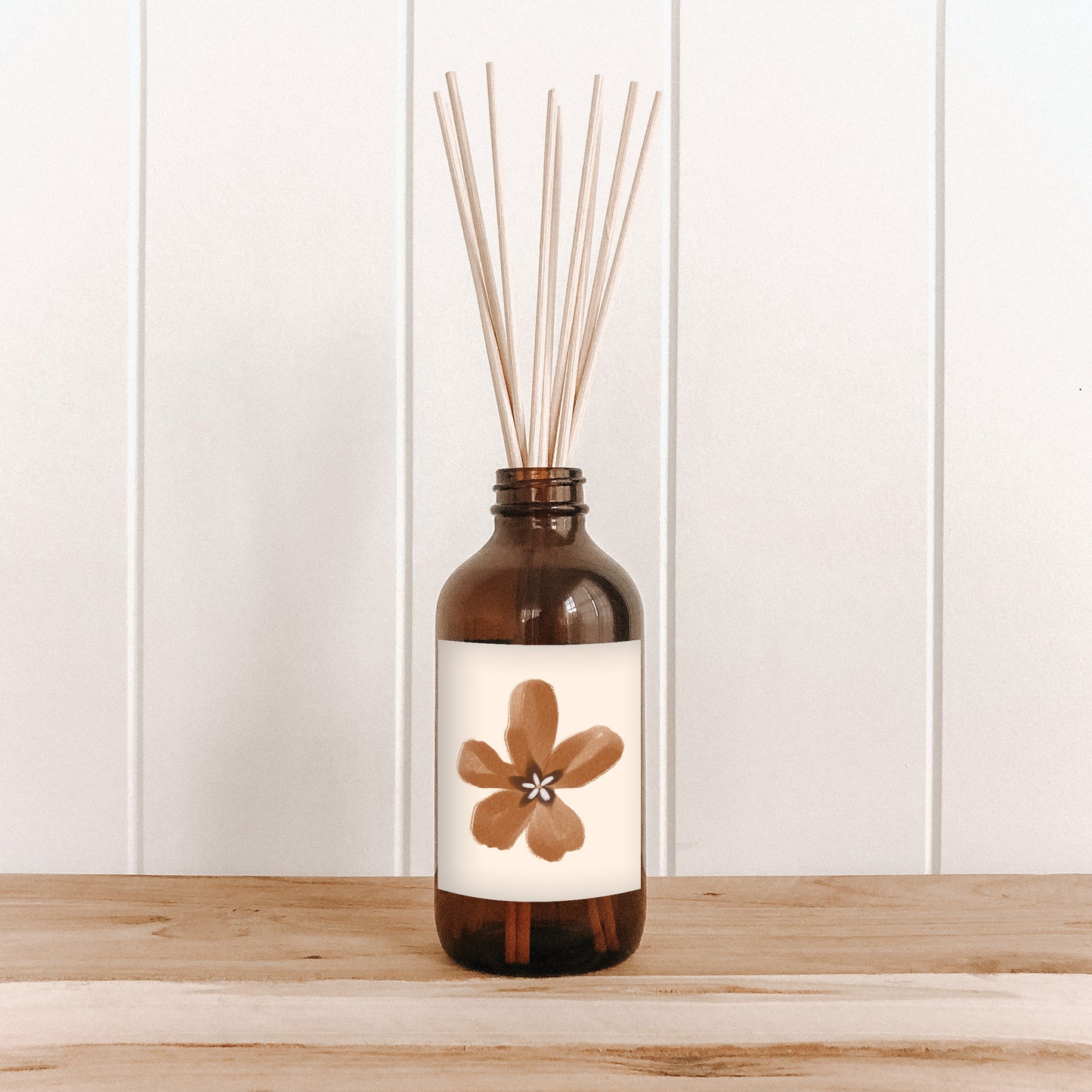 The Commonfolk room diffuser with natural bamboo reed sticks in an amber glass bottle features a label with a brown flower design.