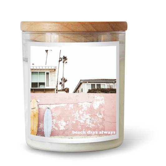 The Commonfolk scented white candle with a wooden lid features an image of a beach scene with palm trees and the text "beach days always" on the label.