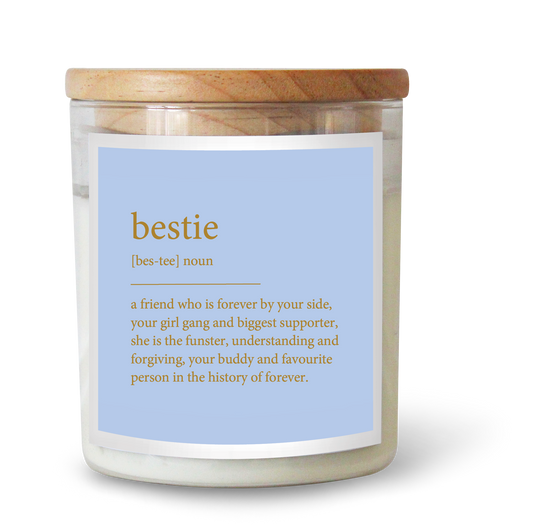 The Commonfolk scented candle has a clear label that defines 'bestie' and features a gold foil design, set in a glass jar with a wooden lid.