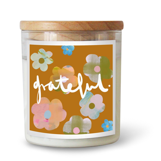 The Commonfolk scented candle features a floral design with various colors such as pink, blue, and green on a yellow background, with the word 'grateful' written across the center.