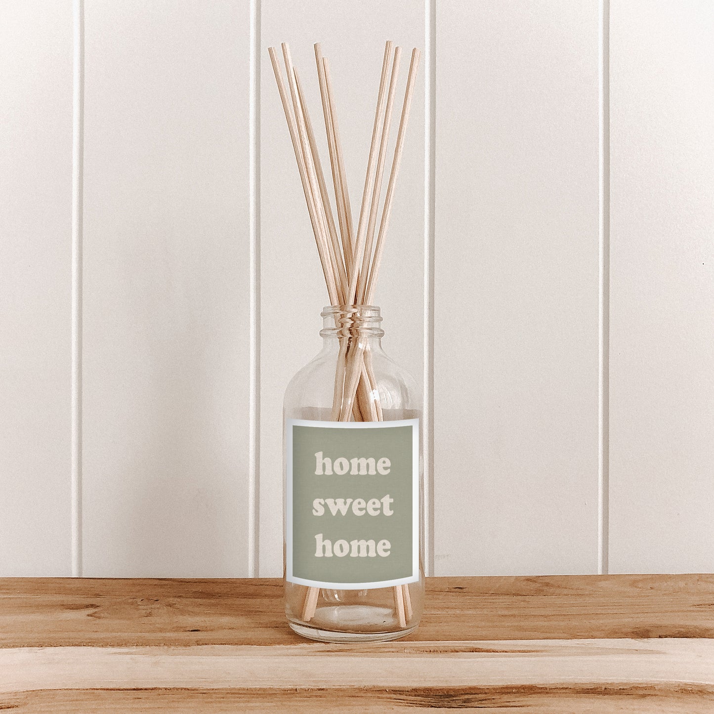The Commonfolk room diffuser with reeds and 'home sweet home' label on a wooden surface and white paneled wall background