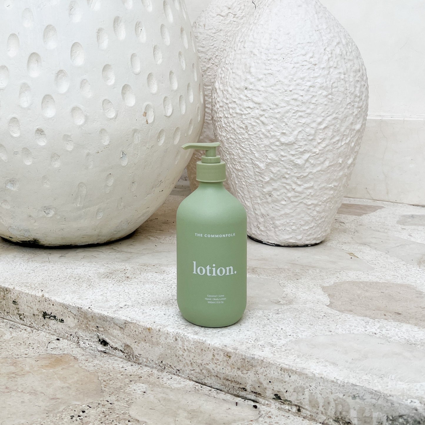 Matte green lotion in a decorative vase is placed on a textured stone floor, creating a serene and elegant atmosphere.