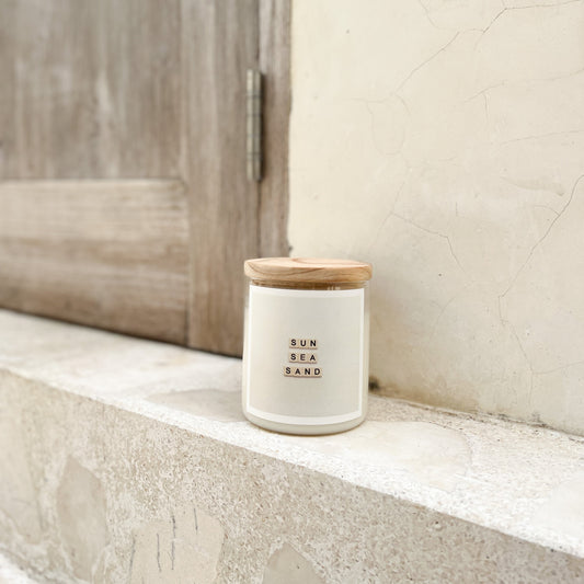 A jar of white wax-scented candle is placed on a ledge, showcasing its smooth surface and simple design.