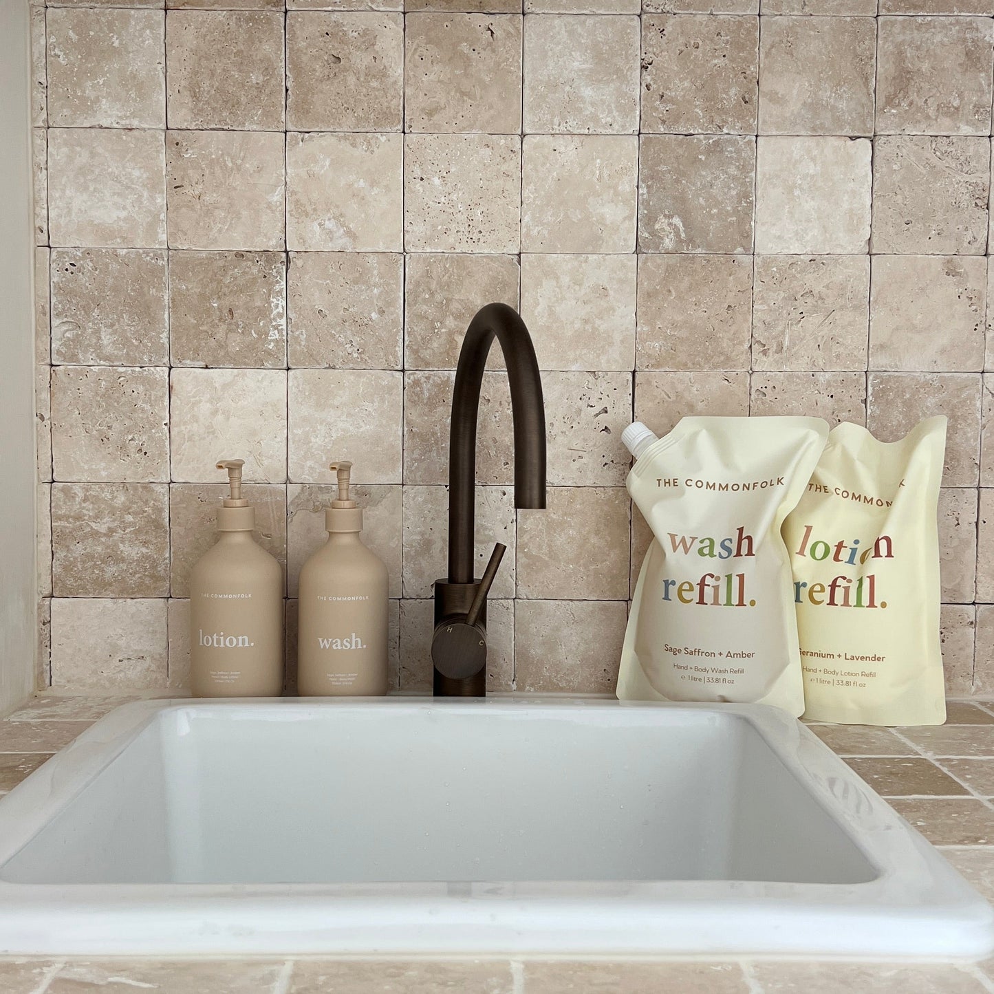 A bathroom sink featuring a faucet, and two bottles of liquid soap, and two refill pouches on the countertop.