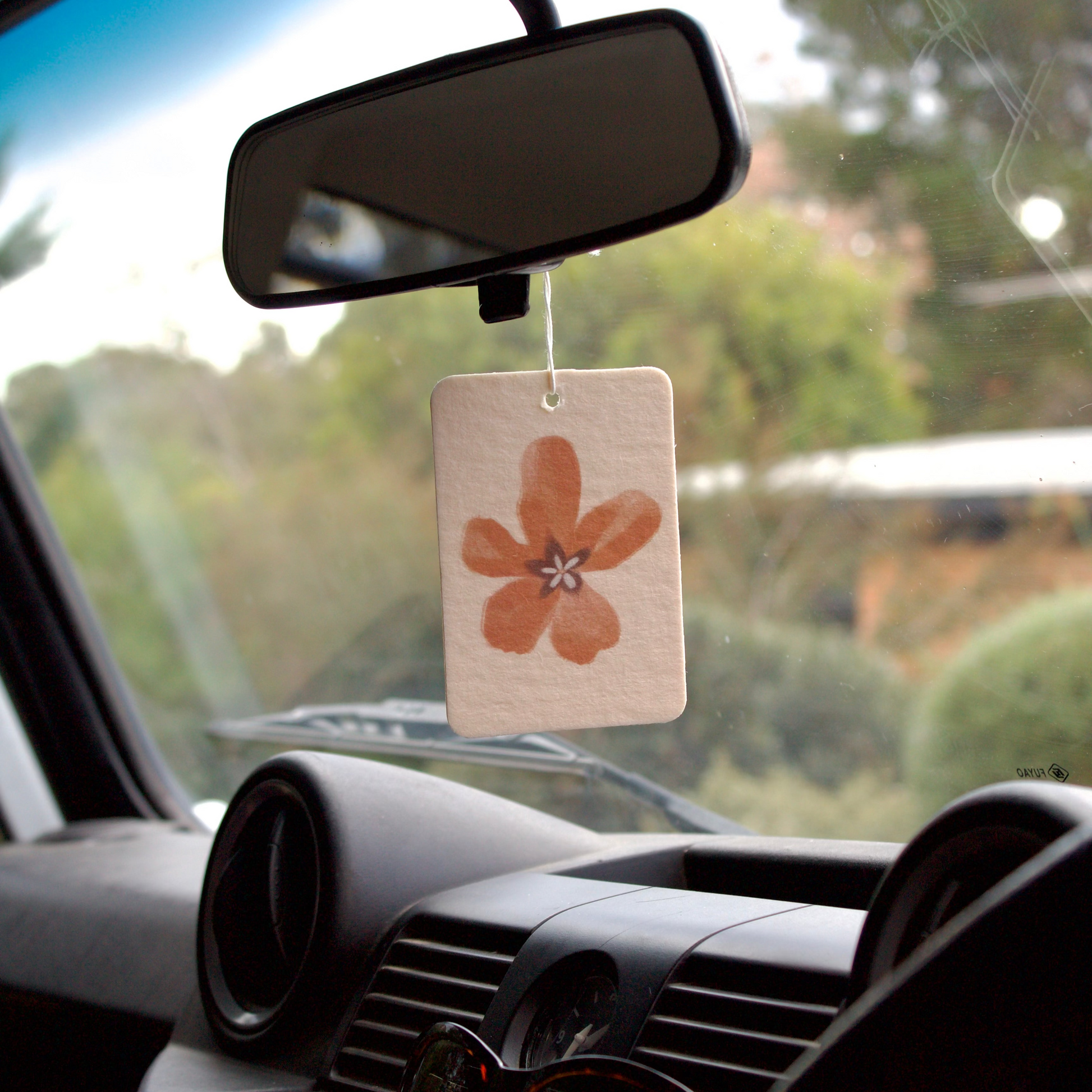 Car air freshener hanging from the rearview mirror with a scenic background