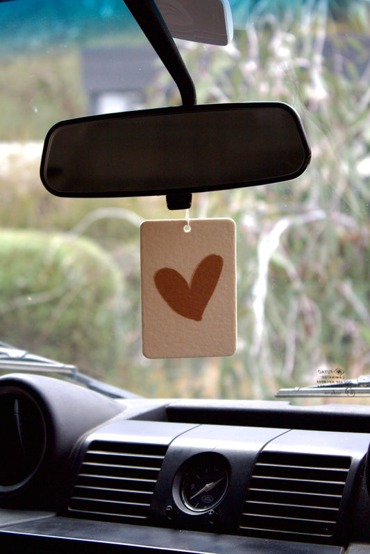 Car air freshener with a heart design hanging from the rearview mirror.