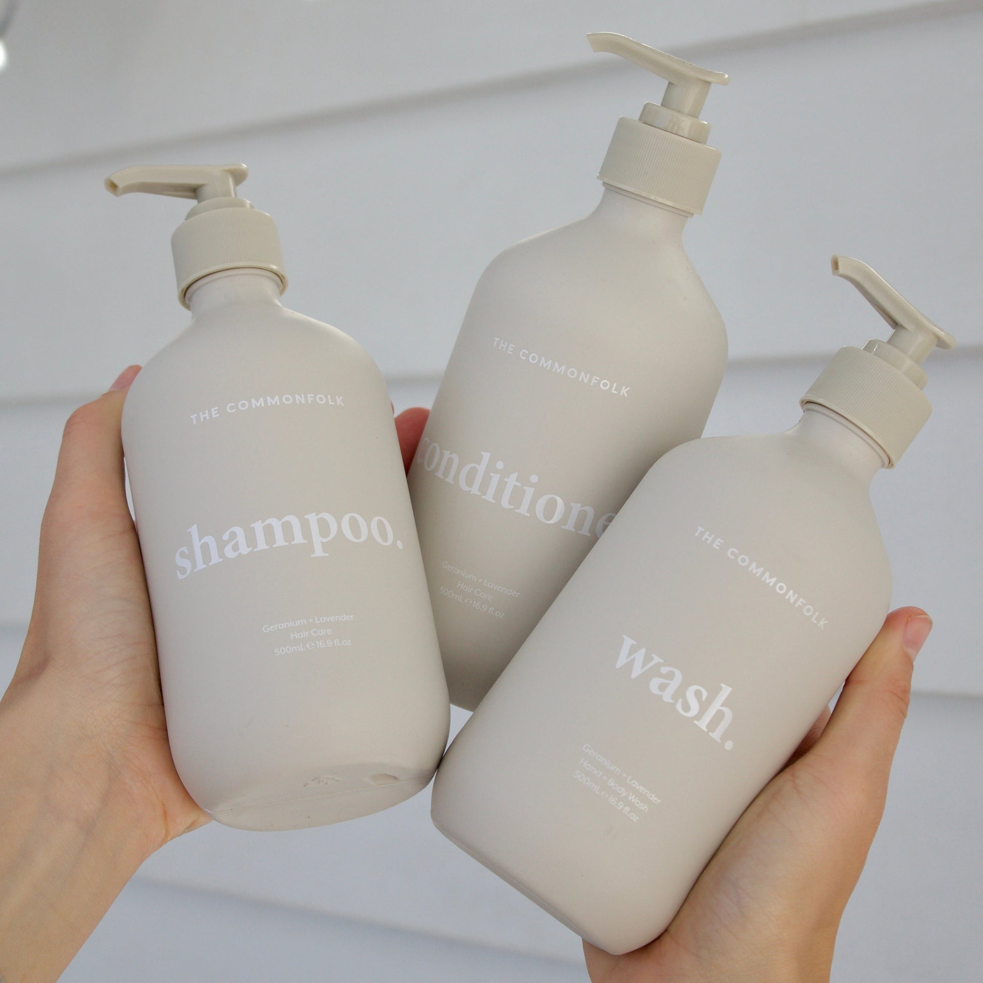 Three bottles labeled 'shampoo', 'conditioner', and 'wash' held by a person against a neutral background.