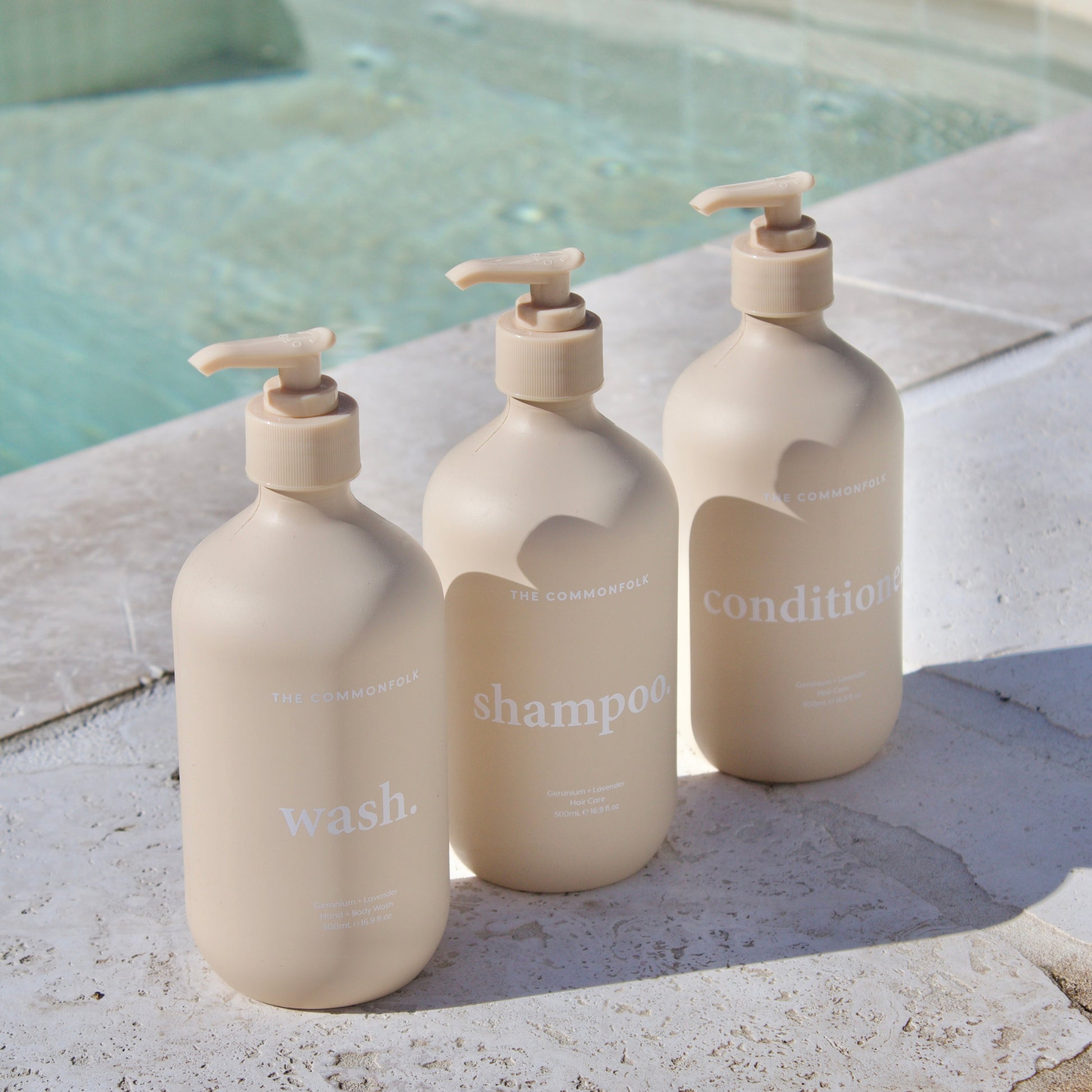 The Commonfolk: Three beige bottles labeled ‘Wash,’ ‘Shampoo,’ and ‘Condition’ by the pool.