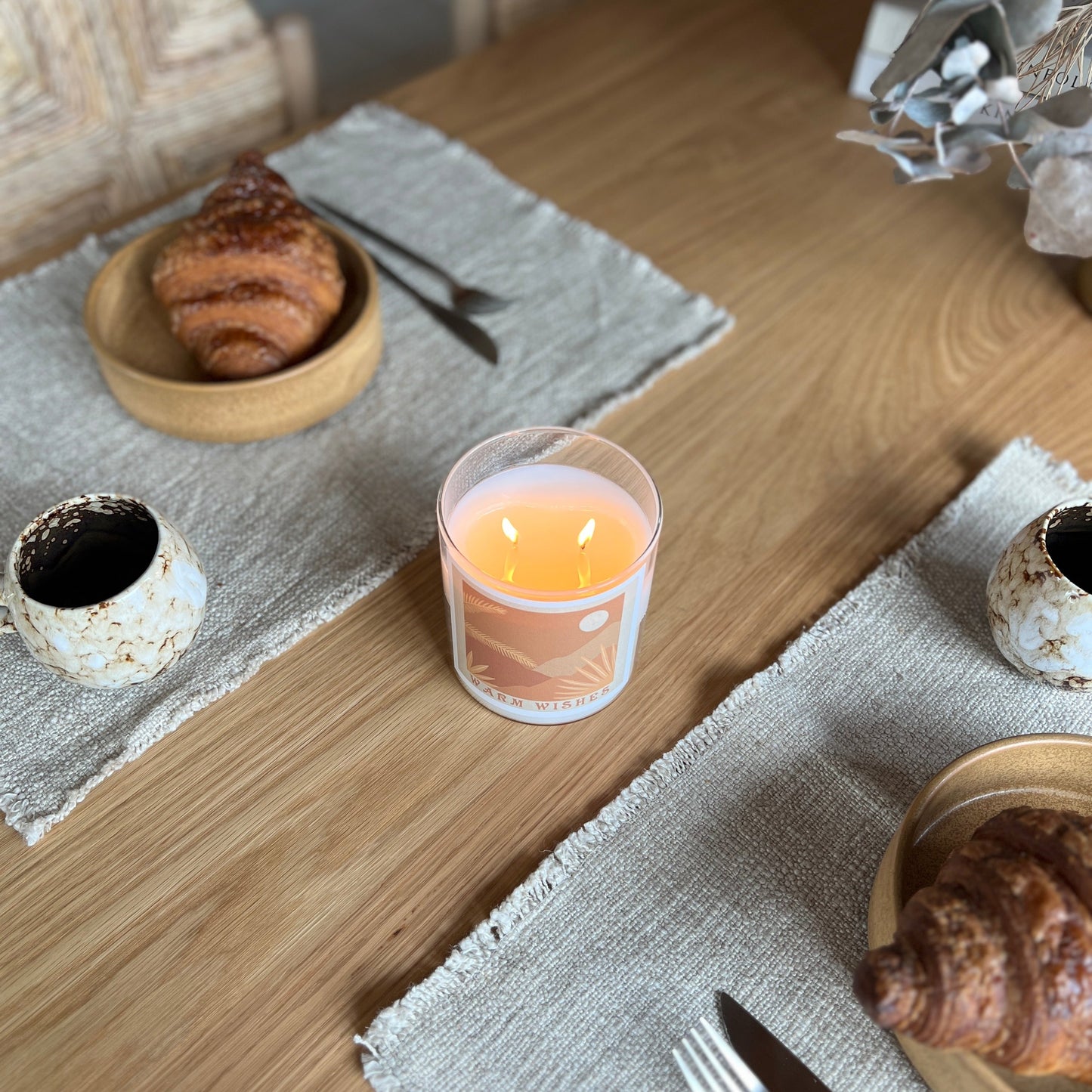 A table set with freshly baked croissants, a steaming cup of coffee, and The Commonfolk scented candle.