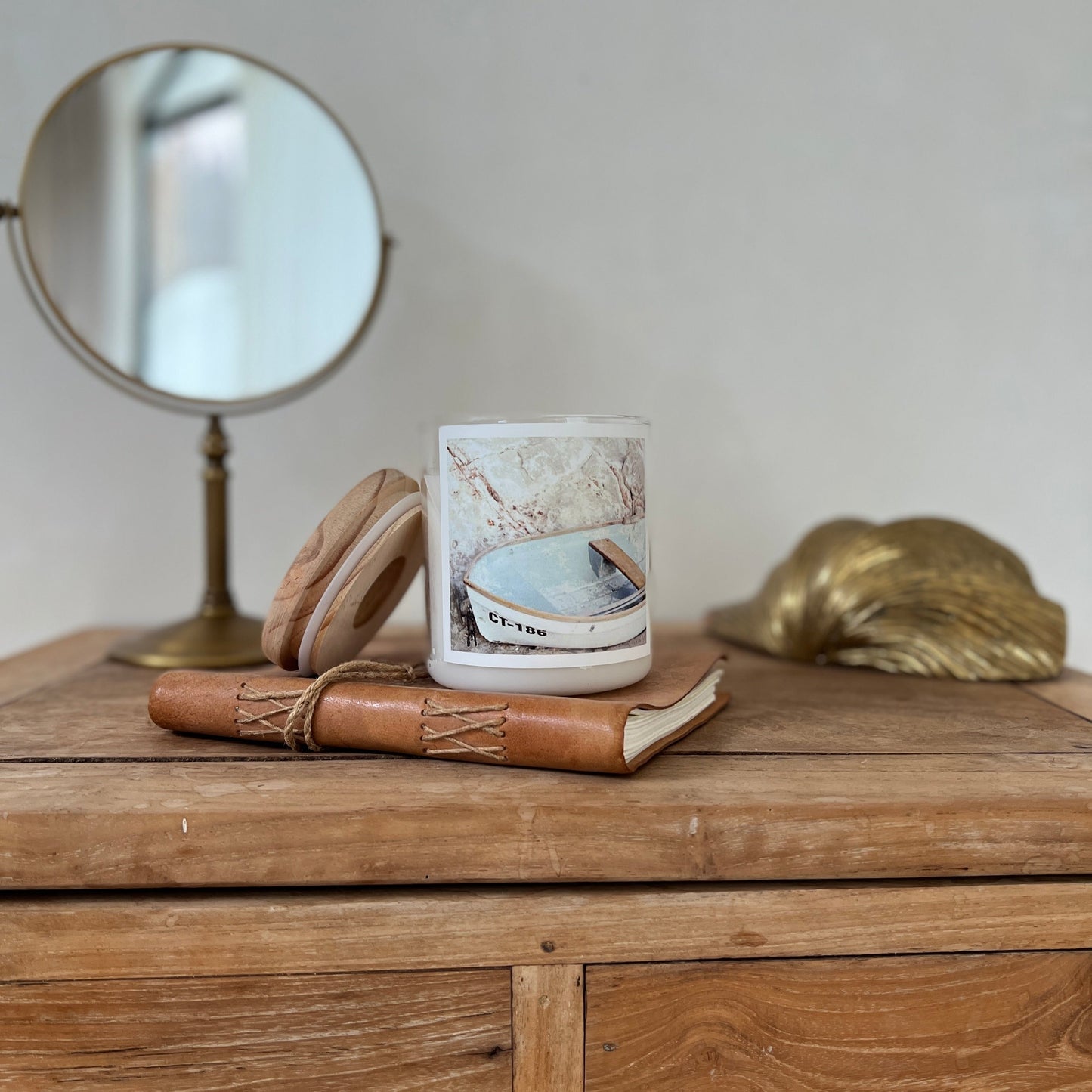 A scented candle at the top of the book and a mirror are arranged neatly on a wooden table.
