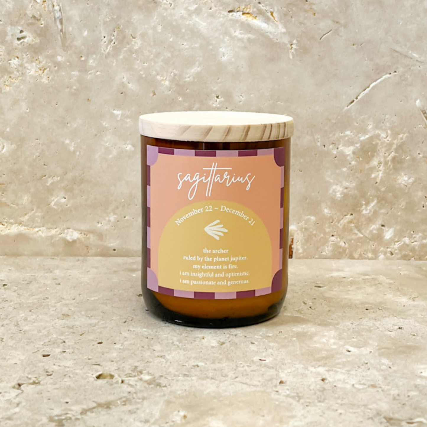 The Commonfolk scented soy wax candle with a label indicating it is a 'Zodiac Colour Candle - Sagittarius' on a marble-textured background.