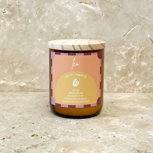The Commonfolk scented candle with a wooden lid and a label featuring the Leo zodiac sign, set against a marble background.