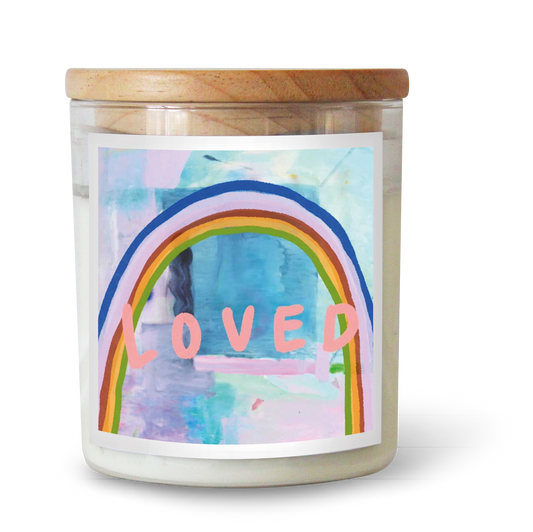 The Commonfolk scented candle has white wax and a clear container, a wooden lid, and a label featuring a rainbow with the word 'LOVED' in the center.
