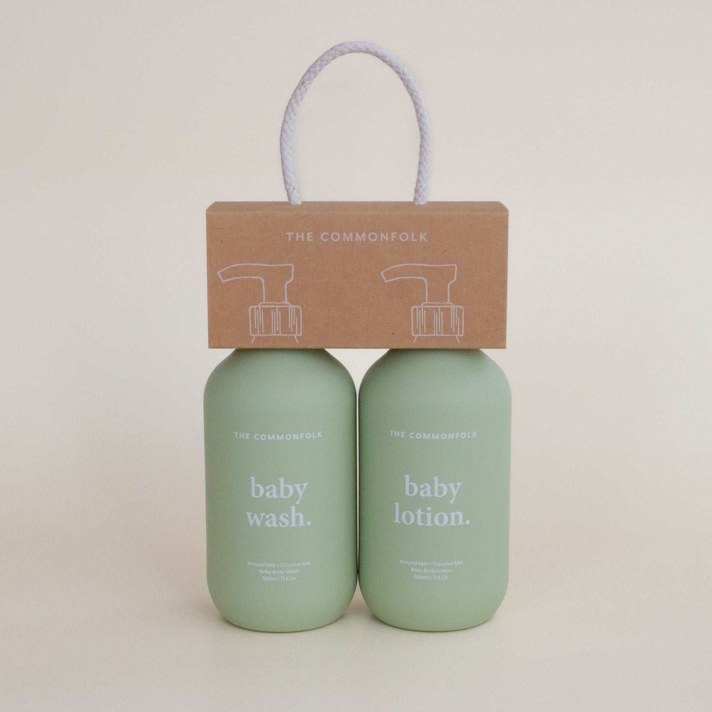 The Commonfolk two matte sage green 500ml bottles labeled 'baby wash' and 'baby lotion', with recycled Kraft carry caddy packaging on top, tied with a string.