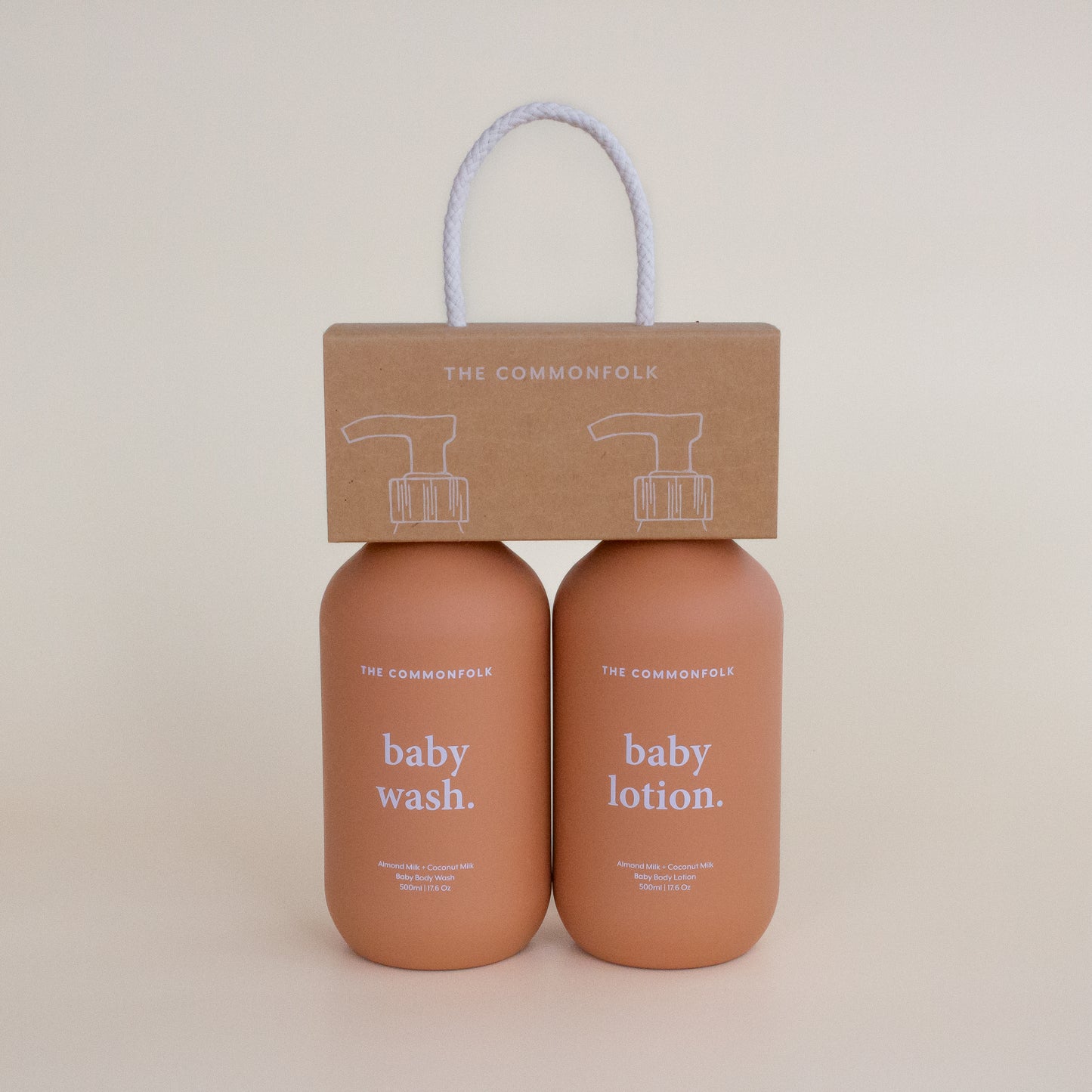 The Commonfolk two terracotta matte 500ml bottles labeled 'baby wash' and 'baby lotion', with a recycled Kraft carry caddy packaging on top.