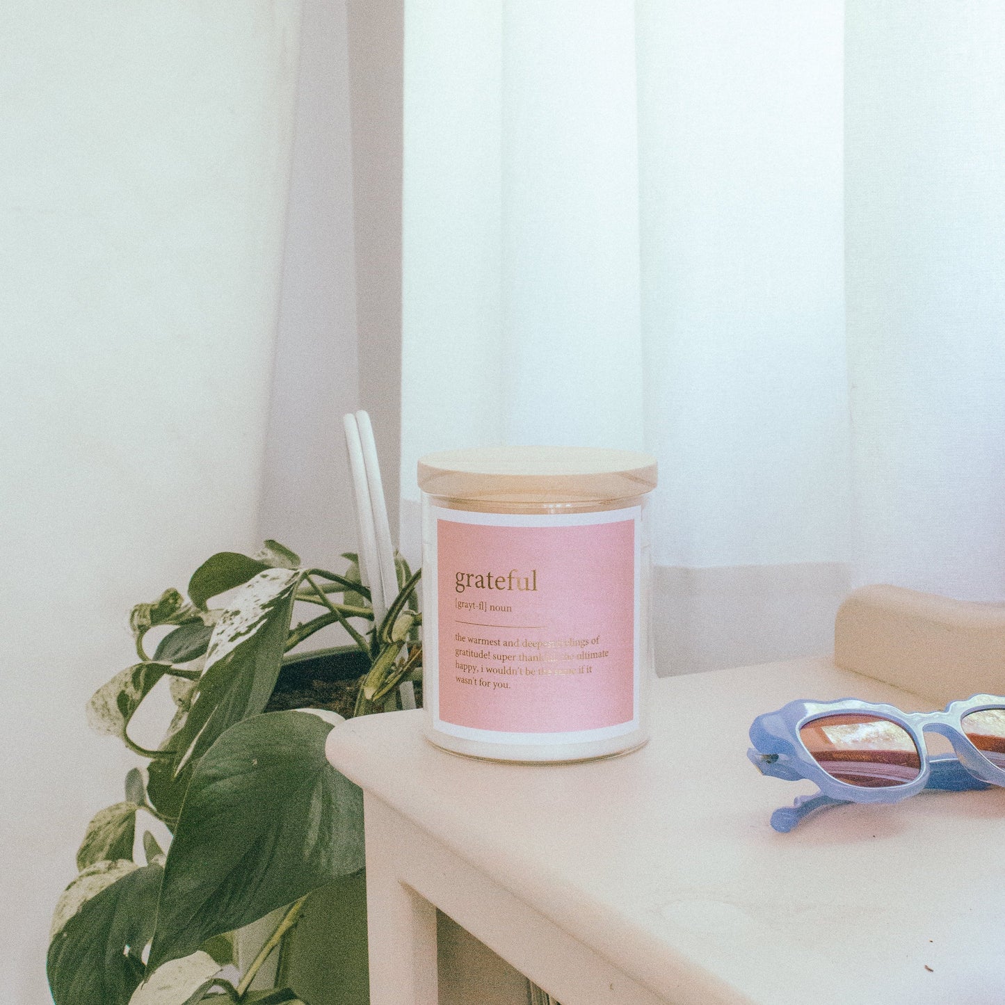 A pink candle, stylish sunglasses, and a small plant arranged on a wooden table.