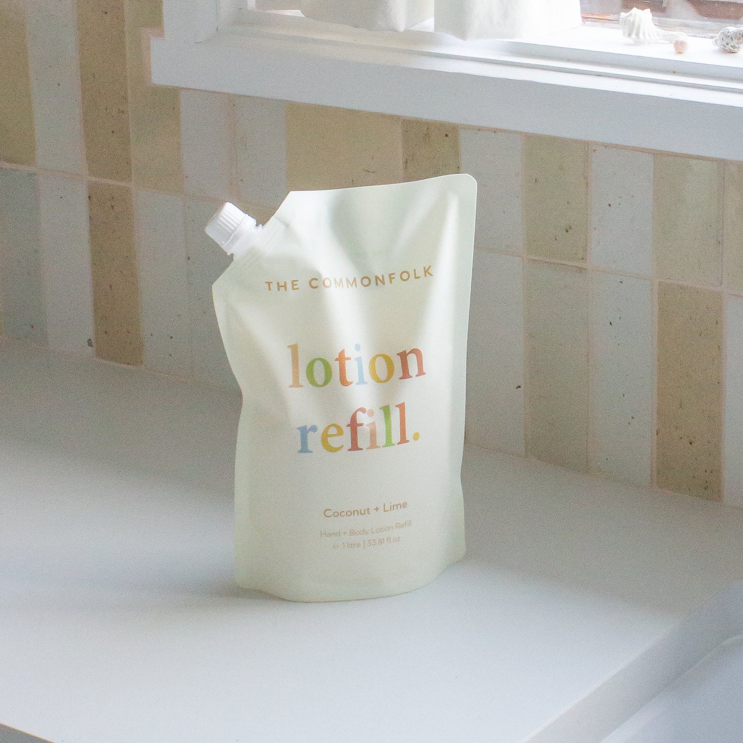 The Commonfolk pouch labeled 'Lotion Refill,' containing 1 liter of hand and body lotion, is placed on a tiled surface.