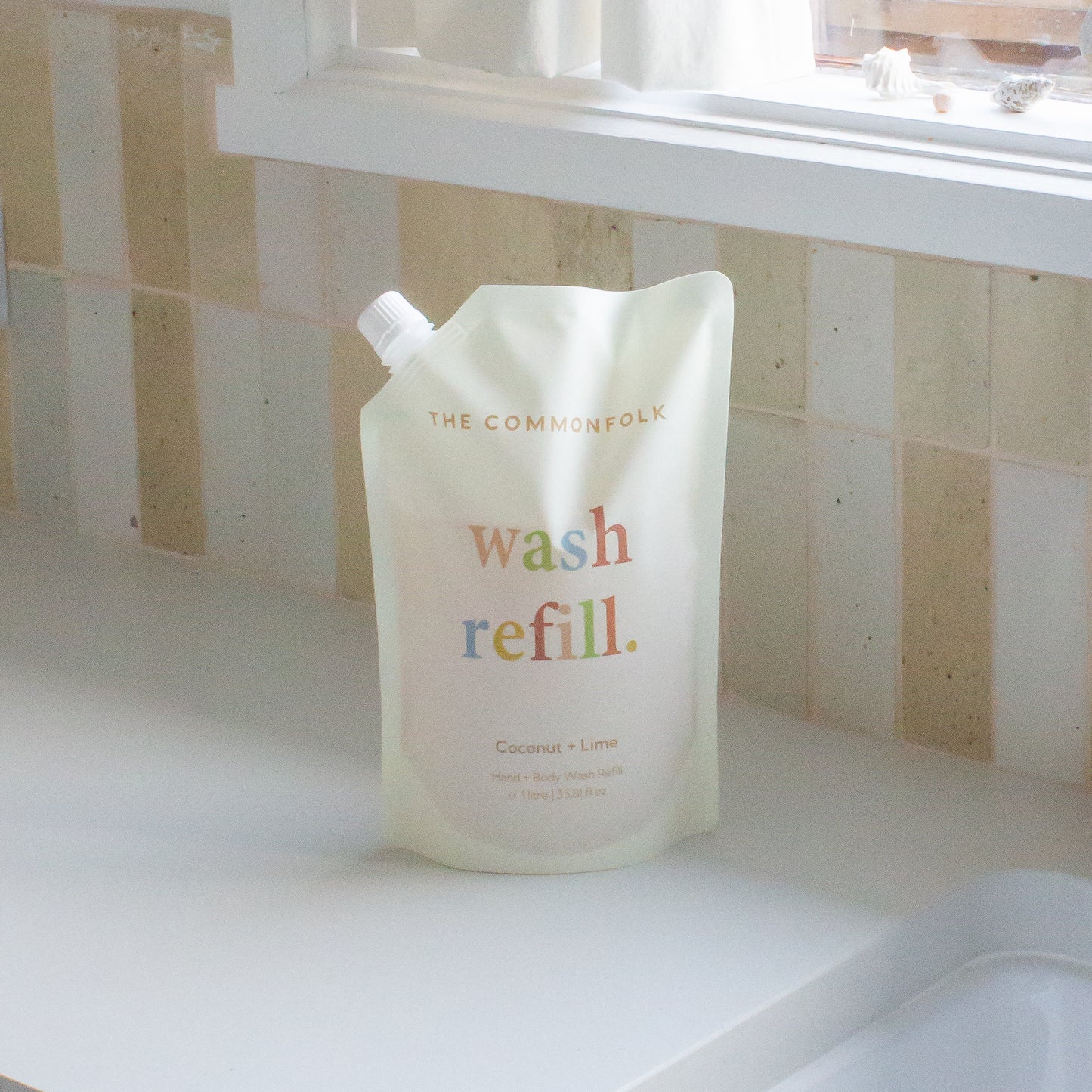 The Commonfolk pouch of 1 liter hand and body wash refill is sitting on a tiled surface, labeled 'wash refill.'