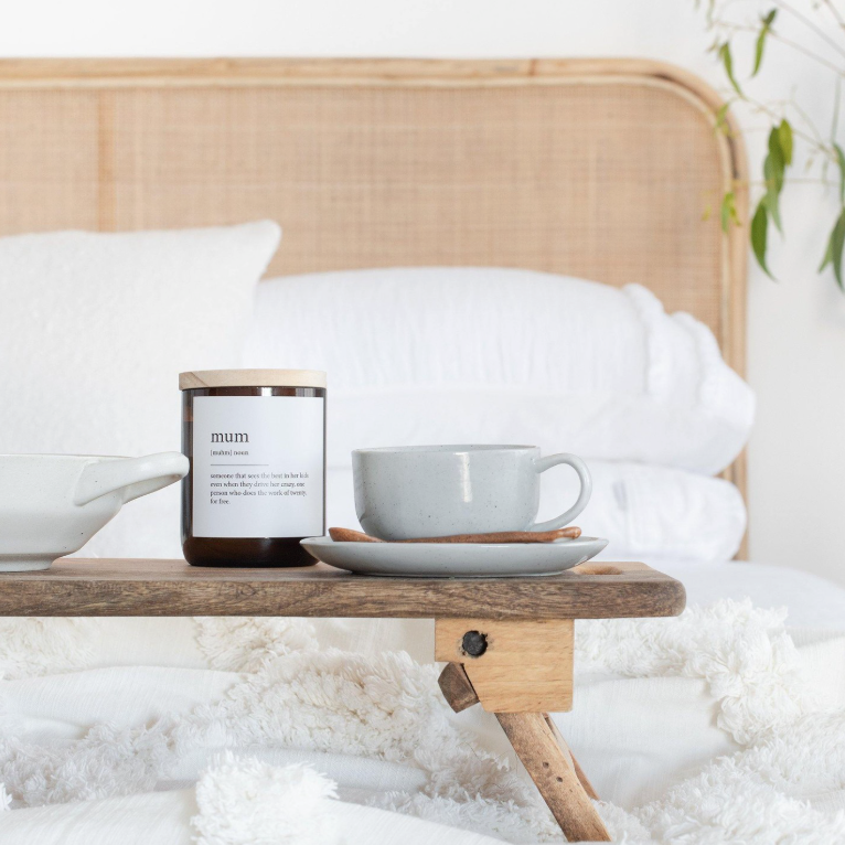 A wooden tray holding a cup and a plate, beside a candle with an amber jar, arranged neatly for serving or display.