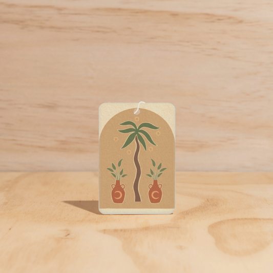 The Commonfolk air freshener features a design with a palm tree and pots, predominantly in beige and green colors.