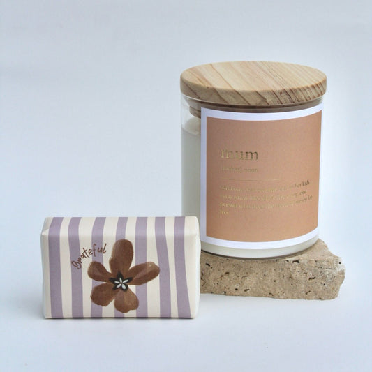 The Commonfolk gift set includes a clear candle jar with the text 'mum' and a wooden lid, a striped body bar with a flower design, all arranged on a stone surface.