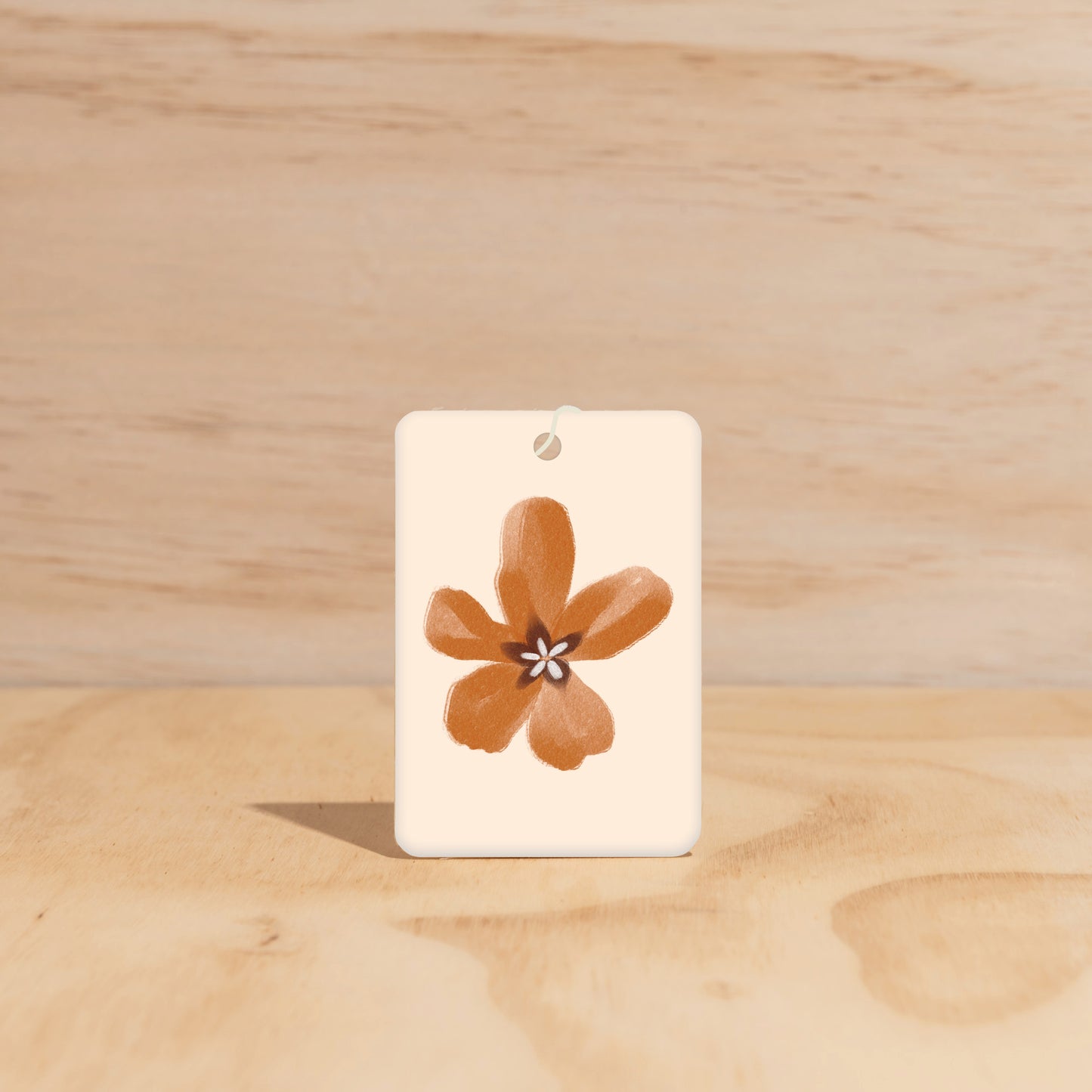 The Commonfolk air freshener white card with a brown floral air freshener attached to it, displayed on a wooden surface.