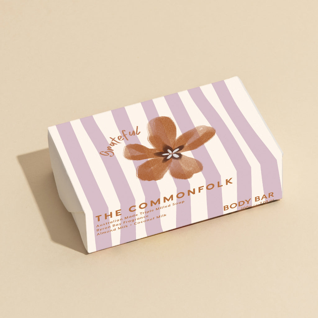 The Commonfolk 200g body bar soap, with striped white and purple wrapping featuring a flower motif.