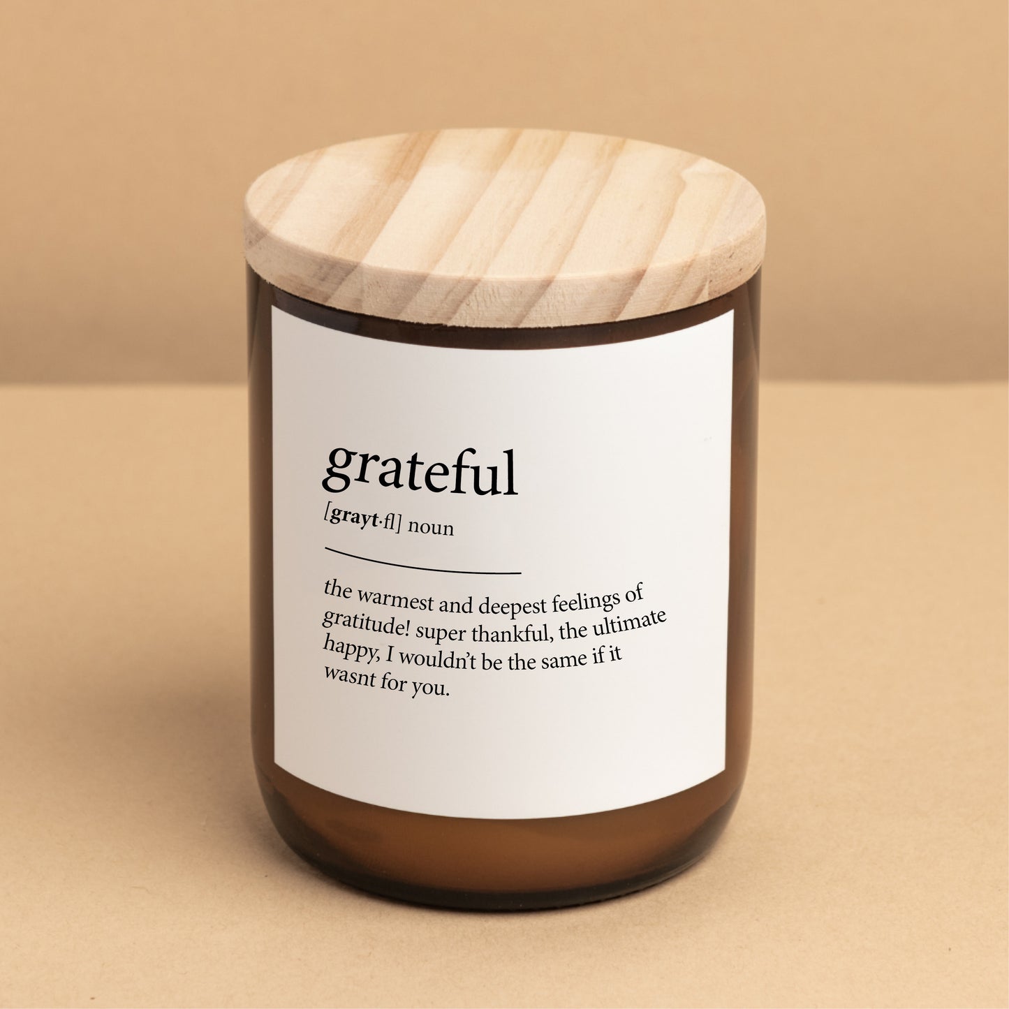 The Commonfolk scented candle with a wooden lid and a label that defines 'grateful' as a warm and deep feeling of great thankfulness.