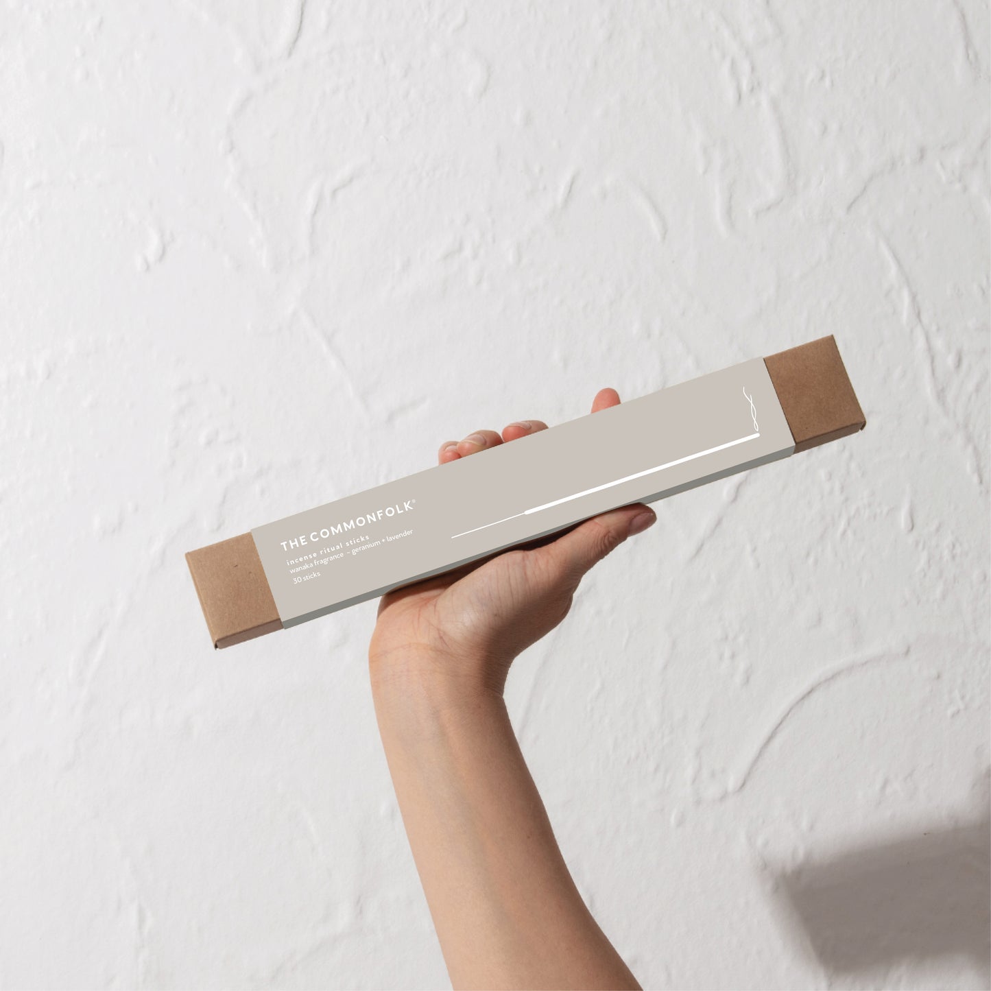 A person is holding a pack of incense sticks against a plain white wall.