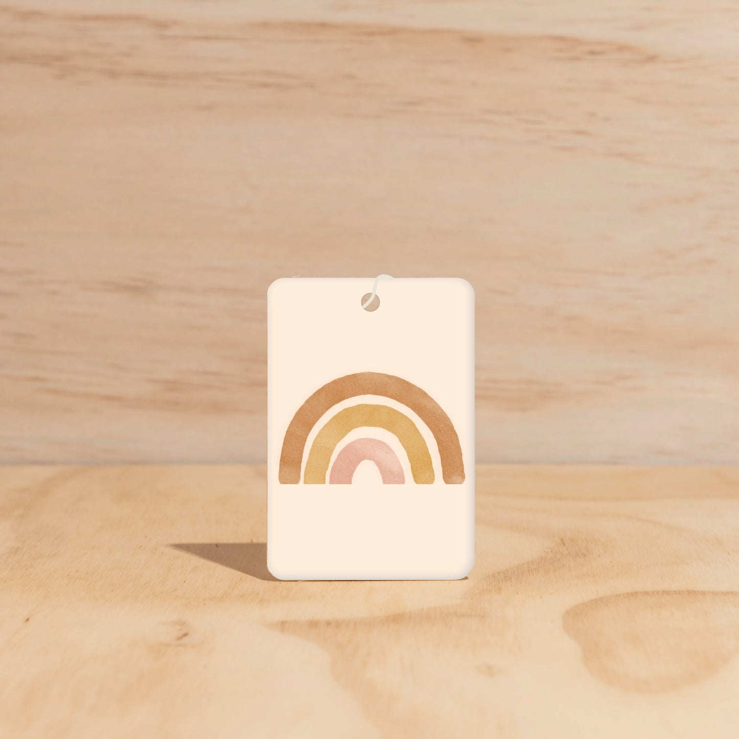 The Commonfolk air freshener, with a rainbow design predominantly in pastel colors, is displayed against a wooden background.
