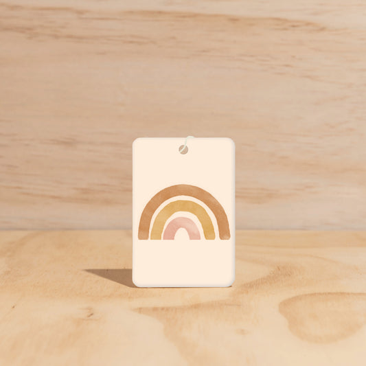 The Commonfolk air freshener, with a rainbow design predominantly in pastel colors, is displayed against a wooden background.