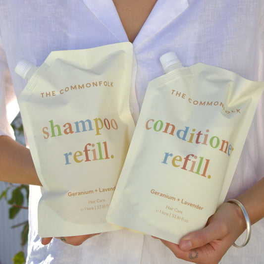 Person holding The Common Good shampoo and conditioner refill packs.
