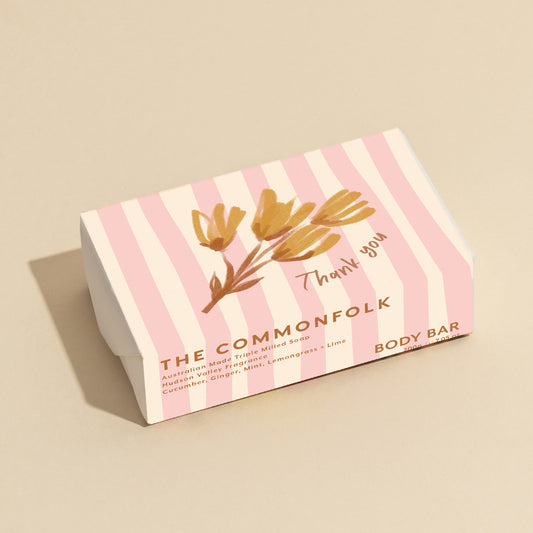 The Commonfolk 200g body bar soap with pink stripes and a floral design, labeled 'Thank you', is placed on a beige background.