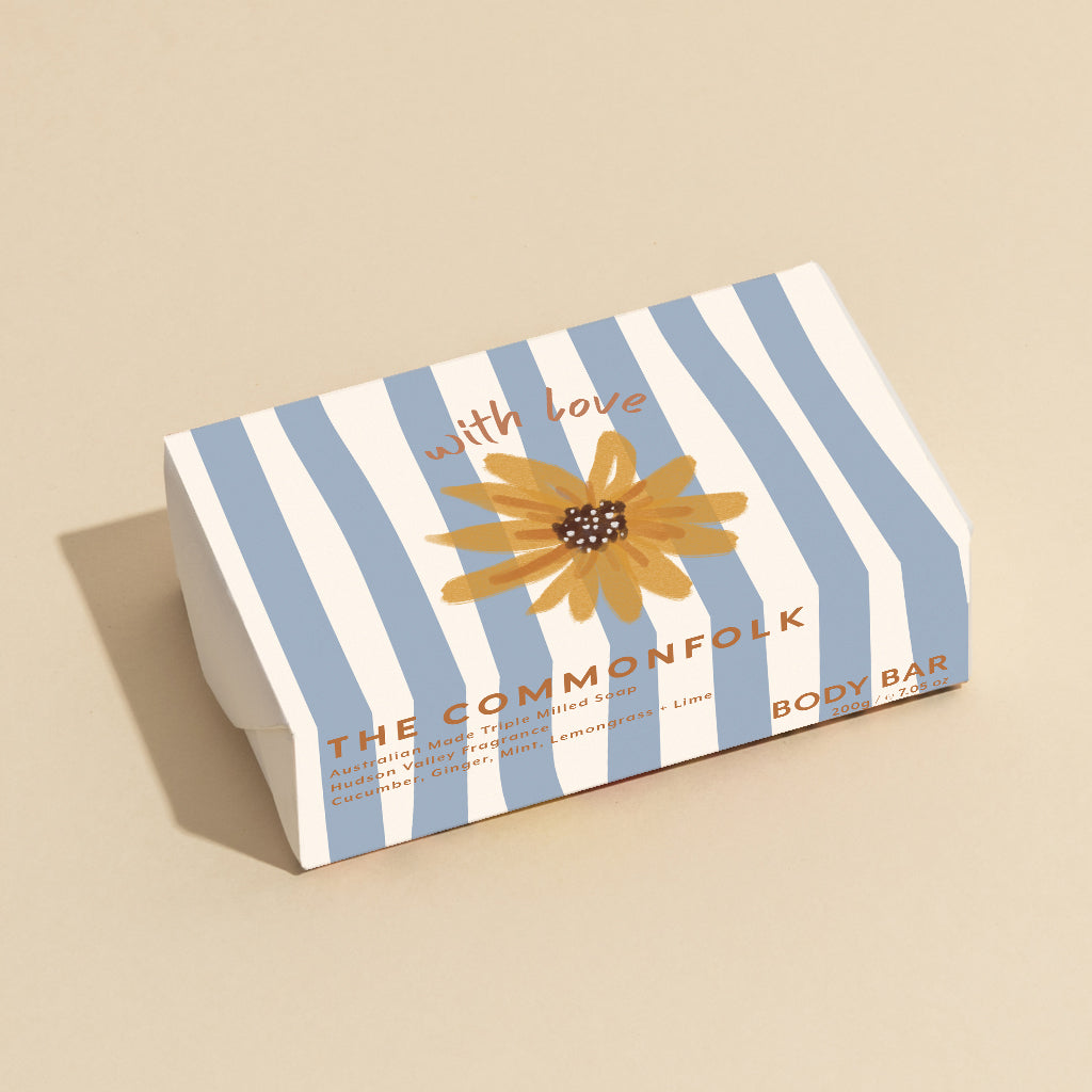 The Commonfolk 200g body bar soap has a striped blue and white design, featuring a sunflower motif and the text 'with love' on the top.