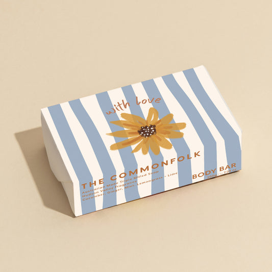 The Commonfolk 200g body bar soap has a striped blue and white design, featuring a sunflower motif and the text 'with love' on the top.