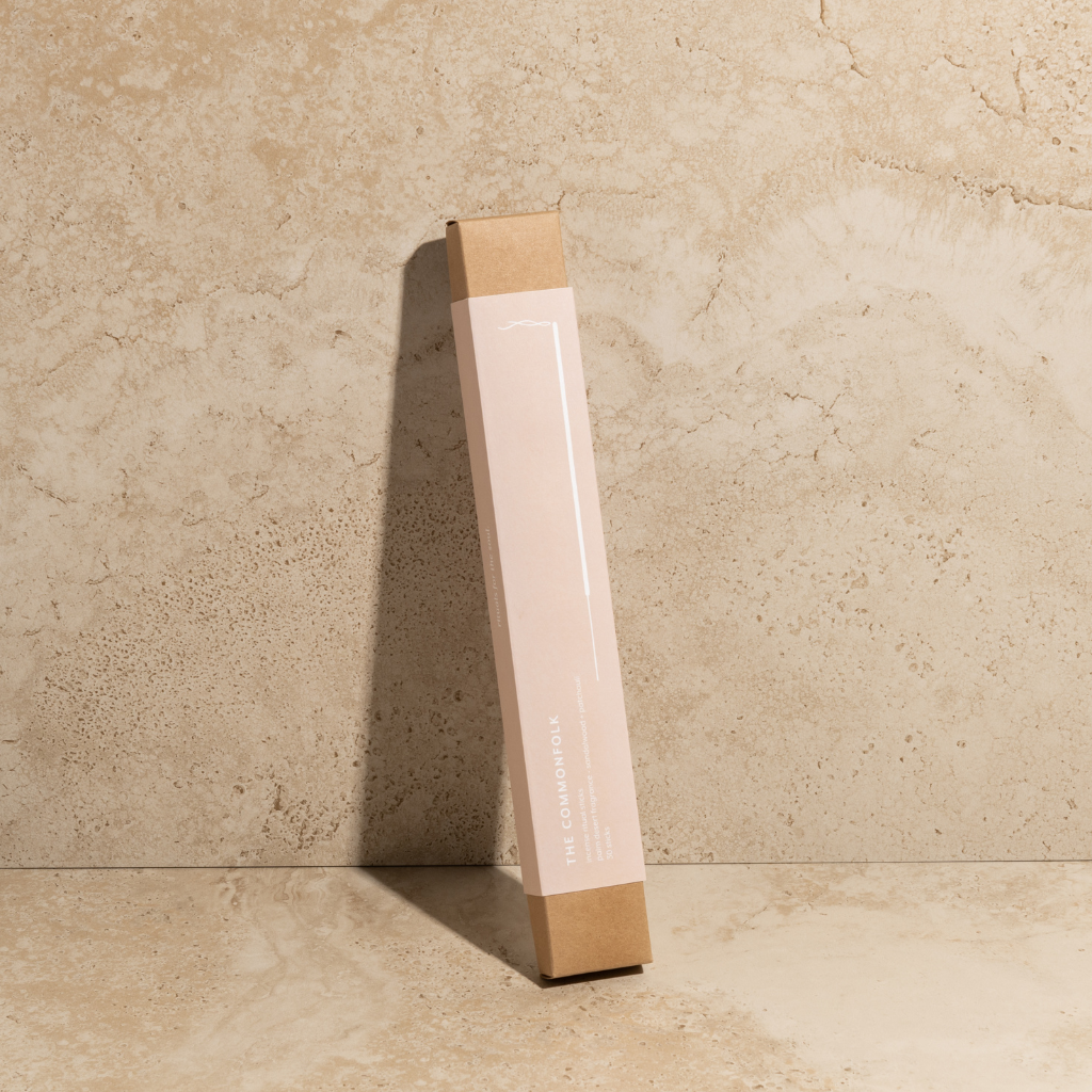 The Commonfolk scented incense ritual sticks pack, with a pink body and brown tip, stands upright against a textured beige background.