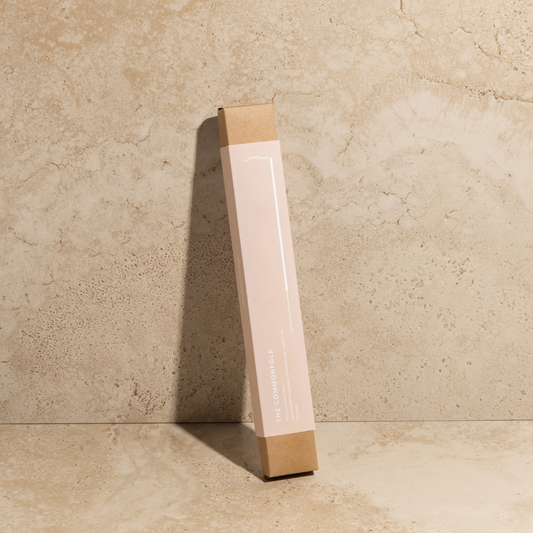 The Commonfolk scented incense ritual sticks pack, with a pink body and brown tip, stands upright against a textured beige background.