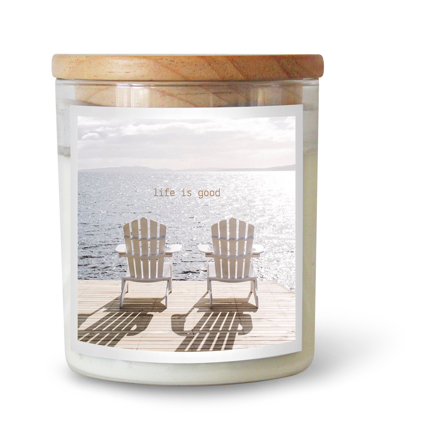 The Commonfolk scented white candle features a label with two wooden chairs on a beach, along with the text 'Life is good' above the image.