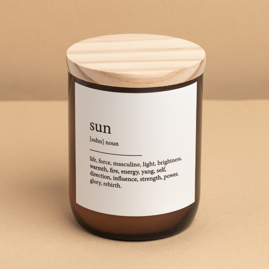 The Commonfolk scented amber glass jar candle with a wooden lid, labeled 'sun' with dictionary definition text.