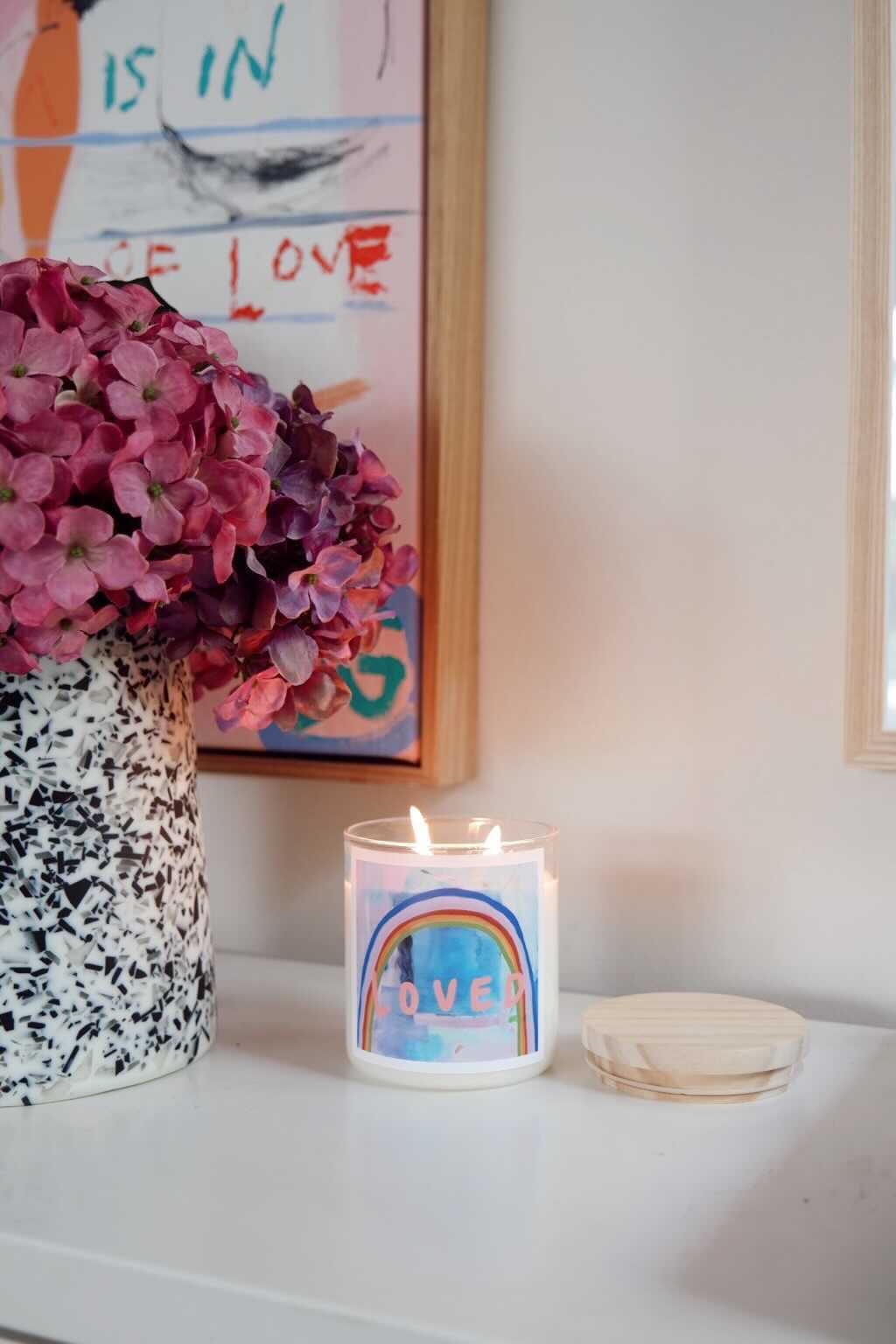 A candle on a white counter beside a colorful painting, creating a serene and artistic atmosphere.