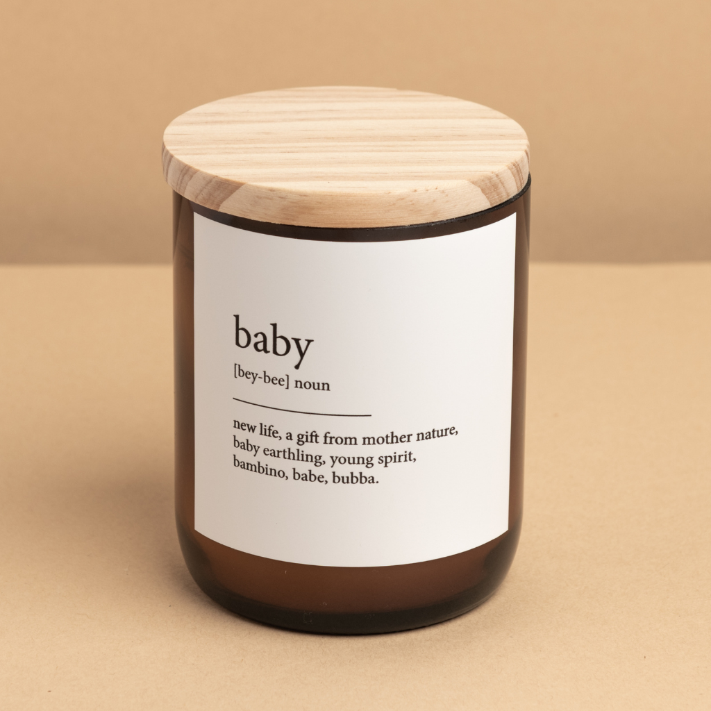 The Commonfolk scented soy candle in an amber jar with a wooden lid, labeled 'baby' along with various definitions.