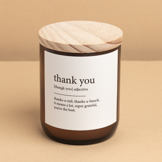 The Commonfolk scented candle has a white label that reads 'thank you' in different fonts, topped with a wooden lid on a beige background.