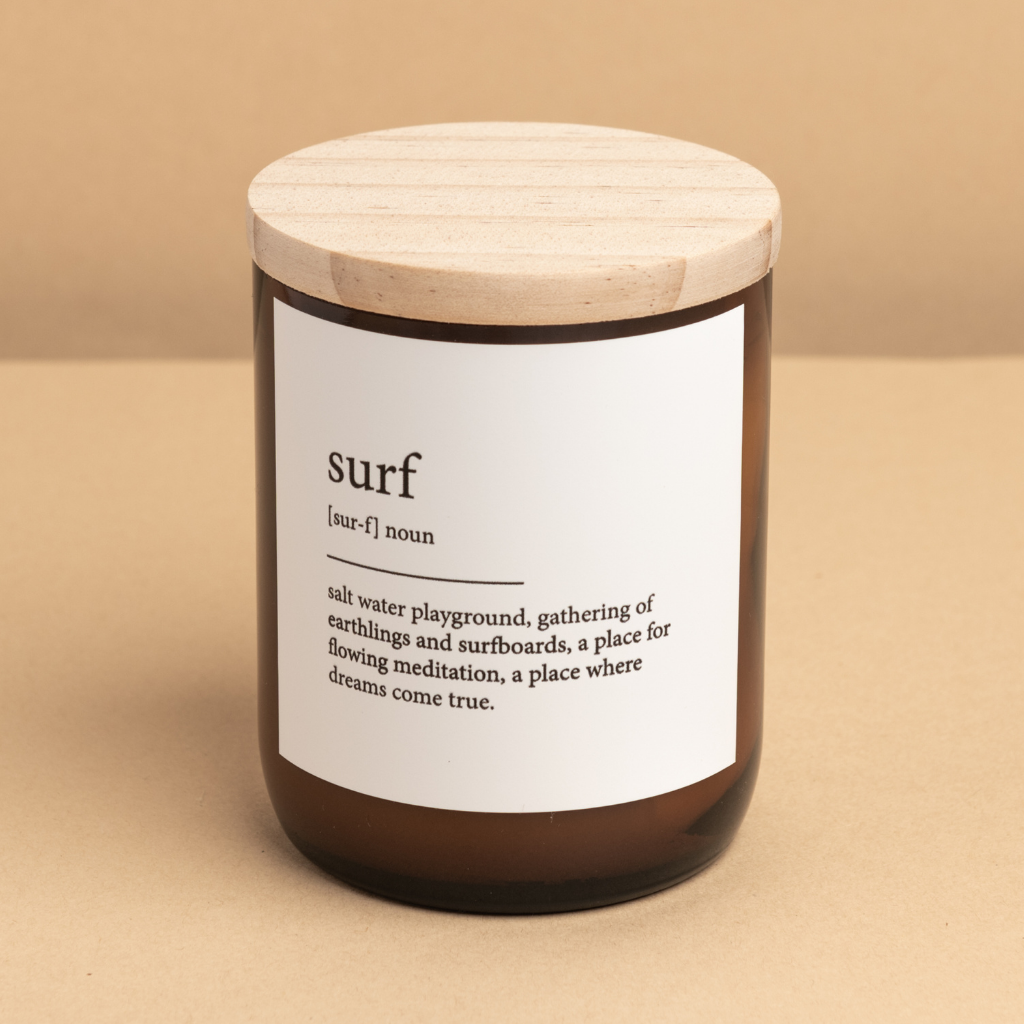 The Commonfolk scented candle has a white label with the word 'surf' defined on it and a wooden lid on a beige background.